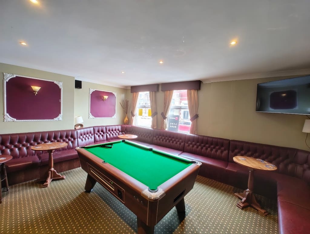 The pool room, a pool table surrounded by leather banquette seating under two windows